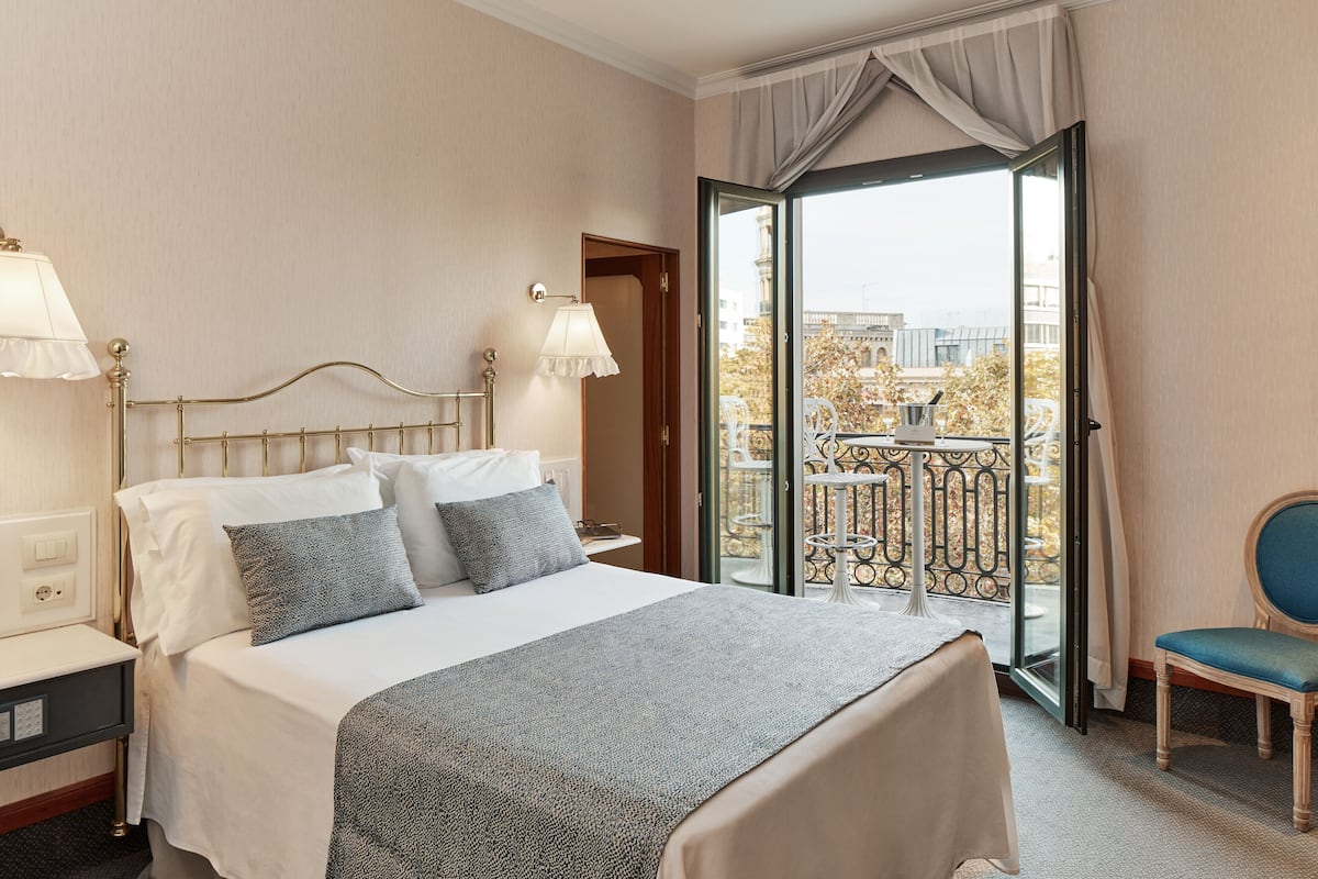 A hotel room with a bed, bedside lamps, a chair, and a balcony with a railing.