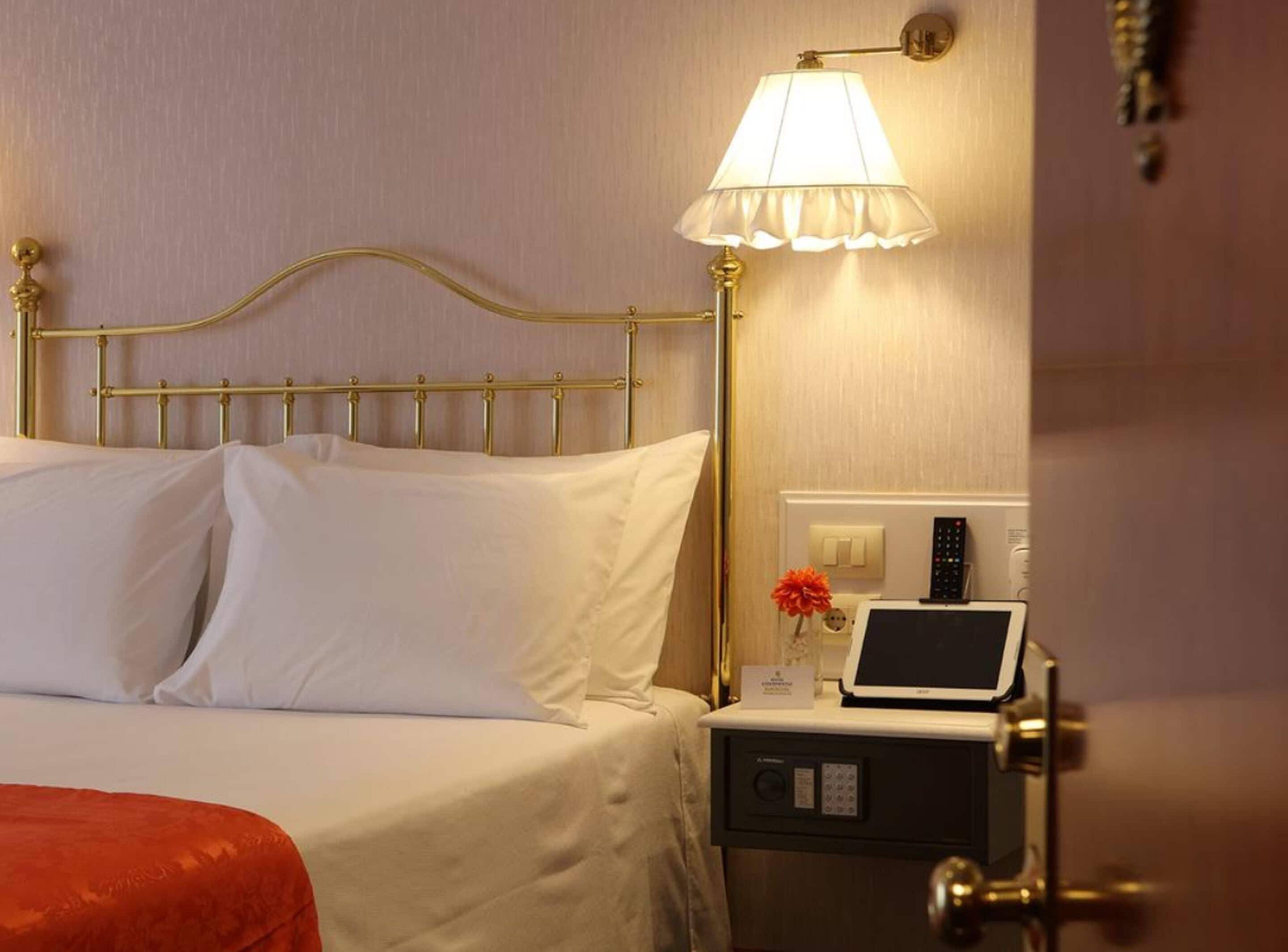 A hotel room with a bed, a bedside table with a lamp, a remote control, and a small card on the table.
