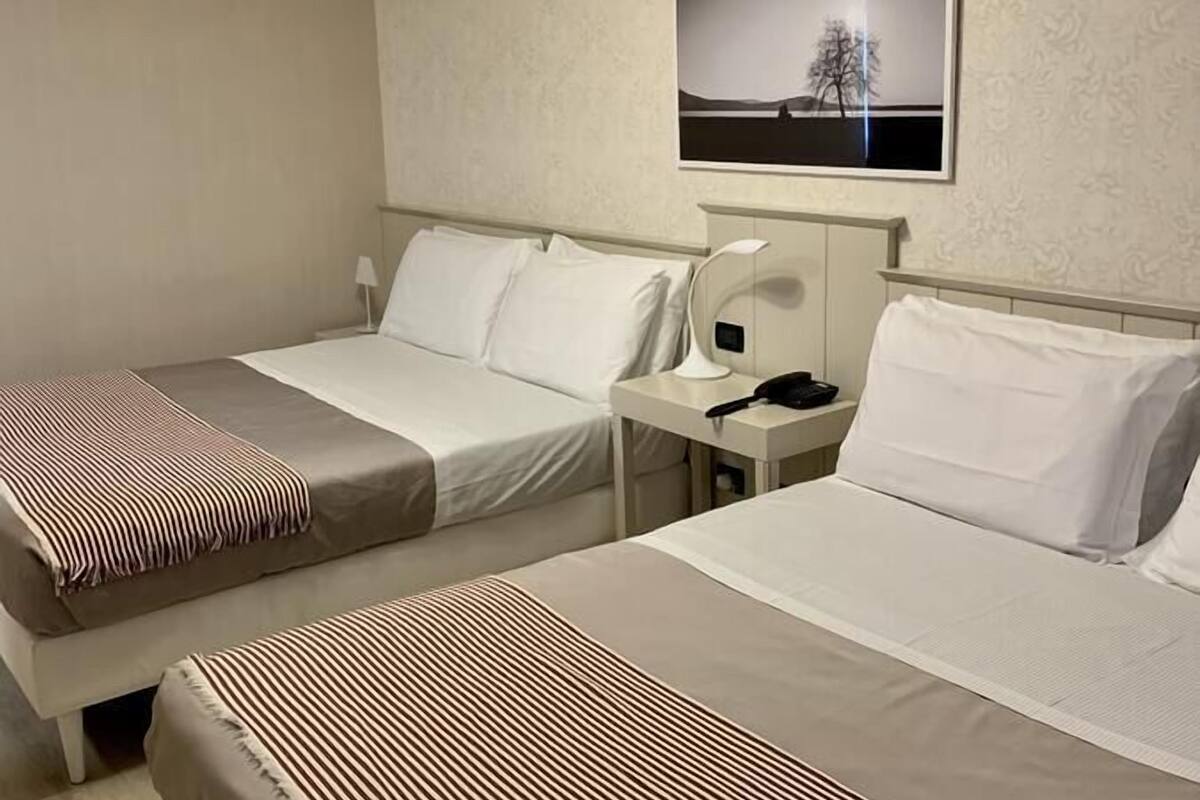 Ein Hotelzimmer mit zwei Betten, einem Nachttisch, einer Lampe, einem gerahmten Bild an der Wand und einer Deckenleuchte.