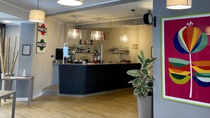 Un área de bar moderna con mostrador, luces colgantes y una obra de arte colorida en la pared.