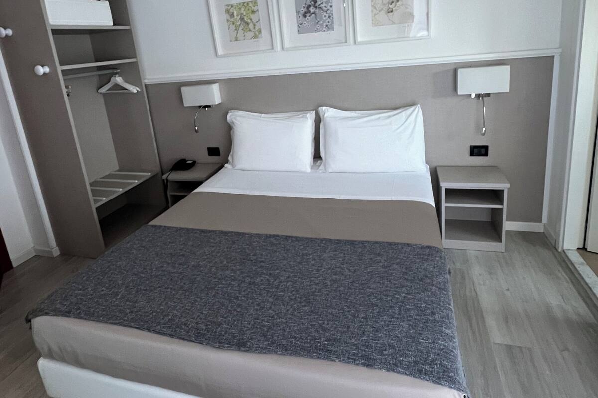 Ein ordentlich eingerichtetes Hotelzimmer mit Bett, Nachttischen, einem Kleiderschrank und Wandbildern.