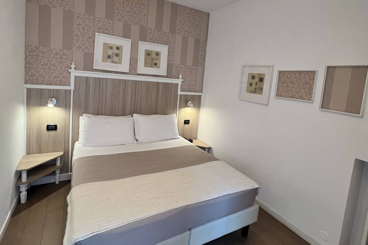 Ein ordentlich eingerichtetes Schlafzimmer mit einem großen Bett, Nachttischen, einer Hängeleuchte und gerahmten Bildern an der Wand.
