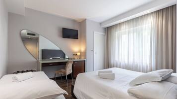 Een hotelkamer met een bed, bureau, stoel, televisie en een groot raam met gordijnen.