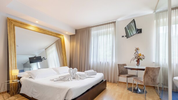 Ein Hotelzimmer mit einem großen Bett, einem Schreibtisch mit zwei Stühlen, einem an der Wand montierten Fernseher und einem großen Spiegel.