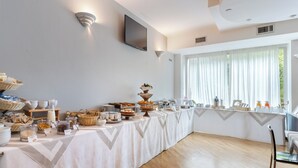 Ein reichhaltiges Frühstücksbuffet mit Speisen und Getränken, ein an der Wand befestigter Fernseher und ein großes Fenster mit Vorhängen.