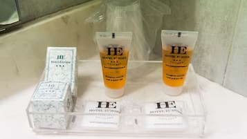 A bathroom with toiletries including Hotel Europa branded shampoo and body gel, and a clear plastic container with additional toiletries.