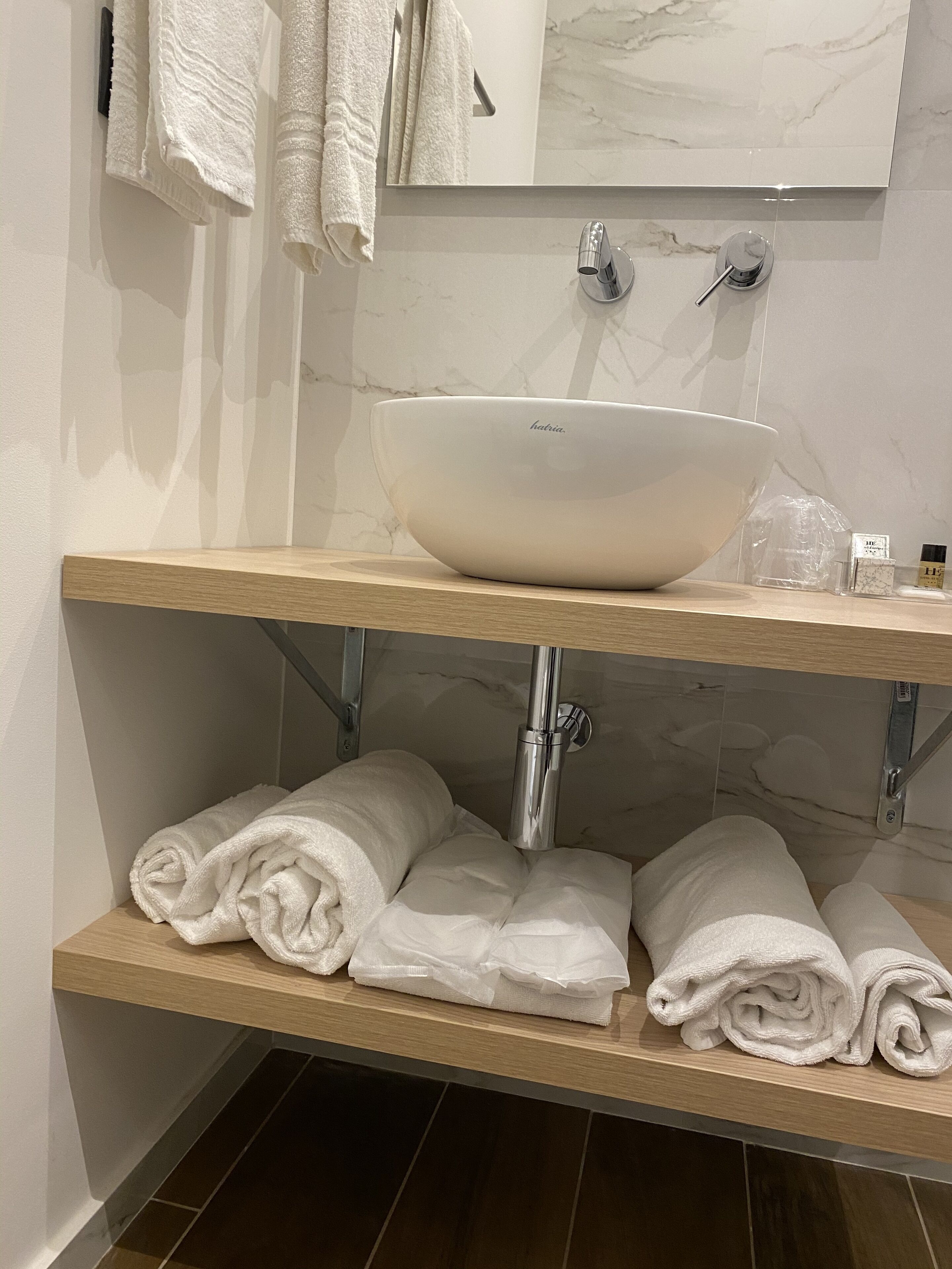 Une salle de bain avec un lavabo en marbre, deux porte-serviettes et une étagère en bois où sont soigneusement pliées les serviettes.