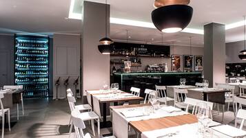 Un interior de restaurante moderno con mesas y sillas blancas, una zona de bar y una estantería para vinos.