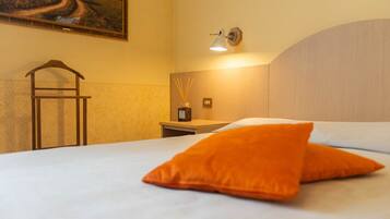 Habitación de hotel con cama, mesita de noche, lámpara, un cuadro en la pared y una silla de madera.