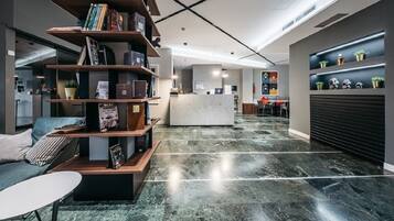 Eine moderne Lobby mit einer Rezeption, einer Holzbibliothek und einer Sitzecke mit einer Couch und einem Tisch.