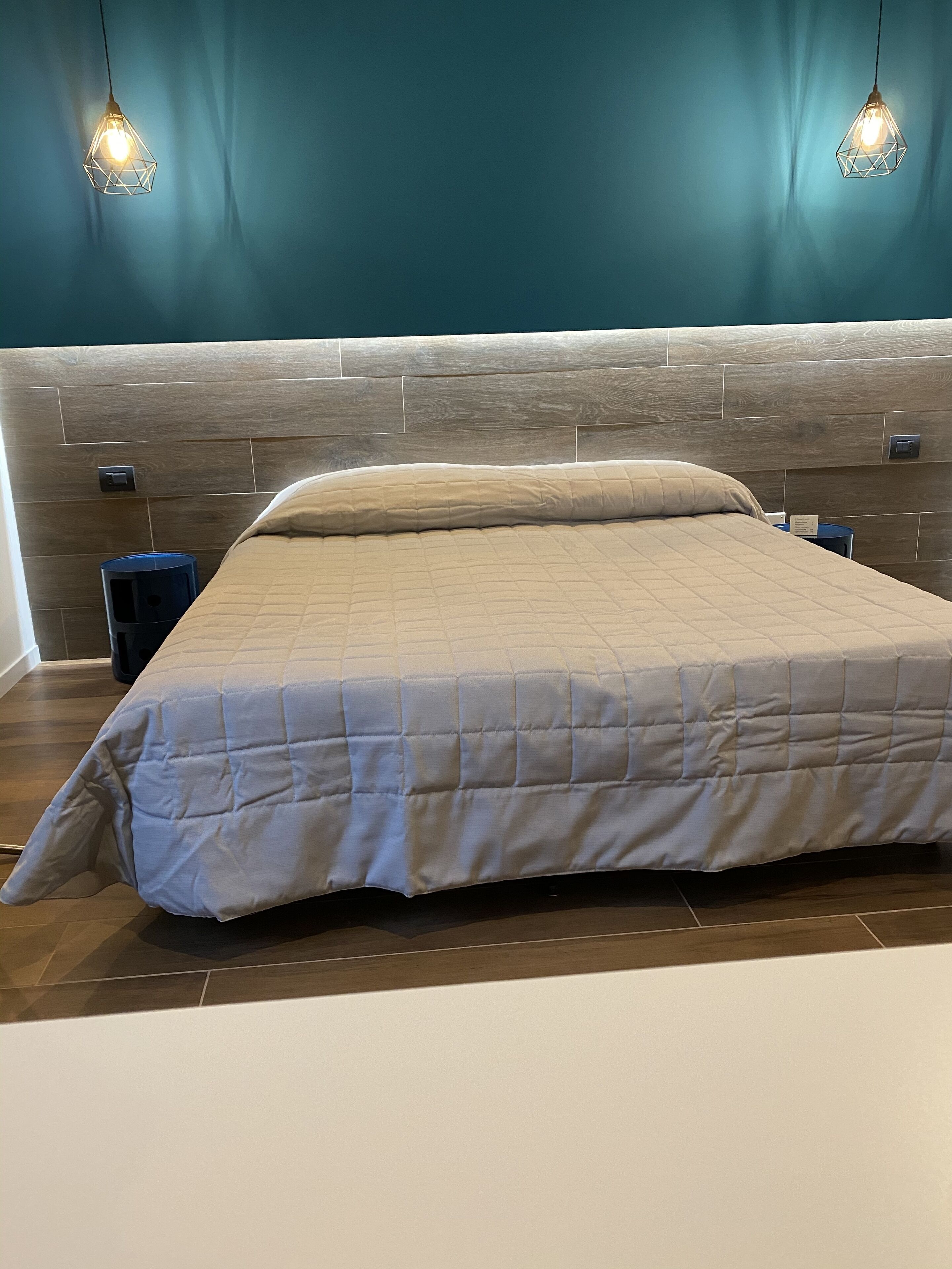 Une chambre à coucher moderne avec une tête de lit en bois, une couvre-lit matelassée et deux lampes suspendues.