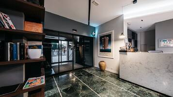 A modern hotel lobby with a marble floor, a reception desk, and a bookshelf with books and decorative items.