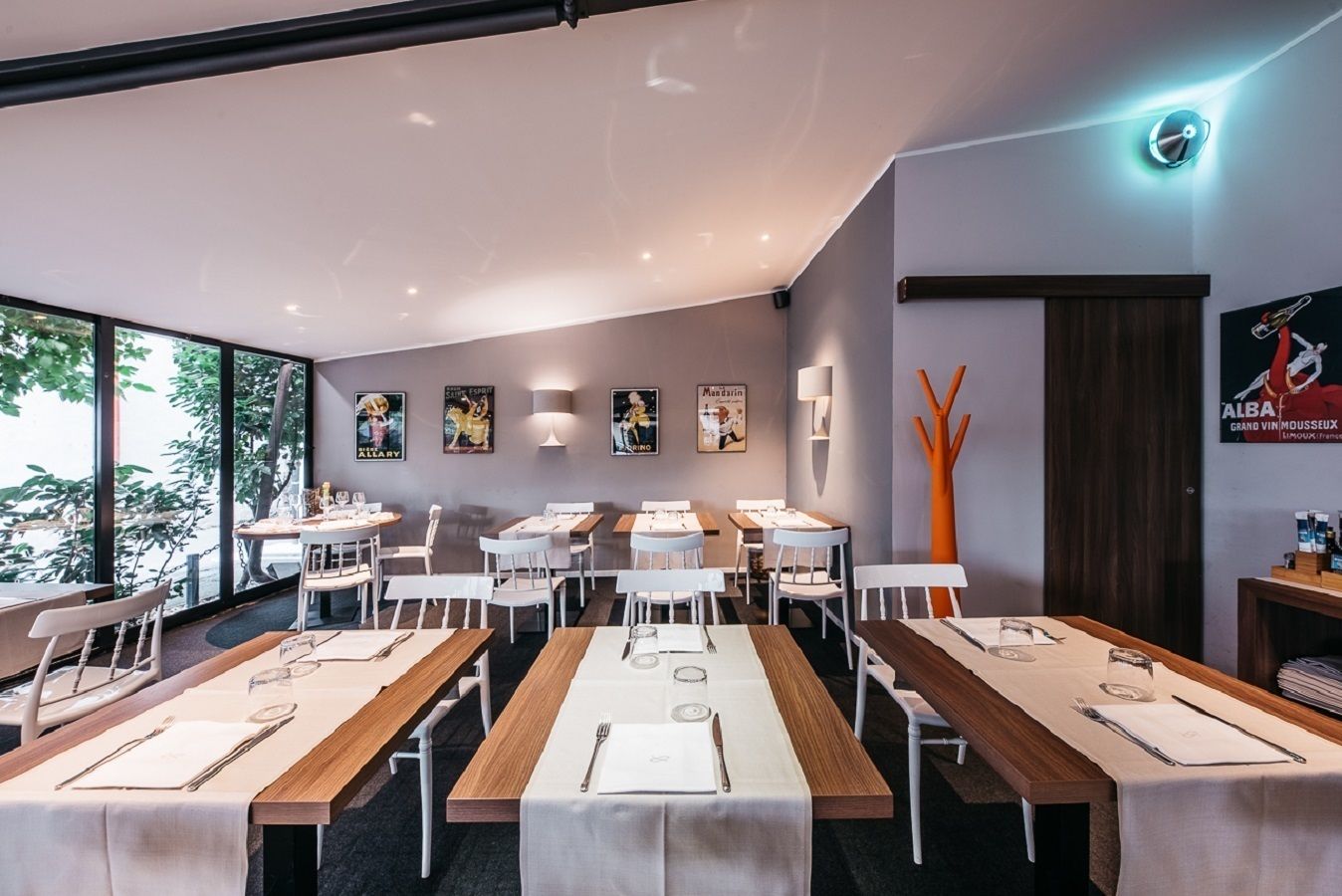 A modern dining area with multiple tables and chairs, large windows, and wall-mounted artwork.