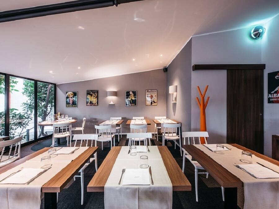 A modern dining area with multiple tables and chairs, large windows, and wall-mounted artwork.