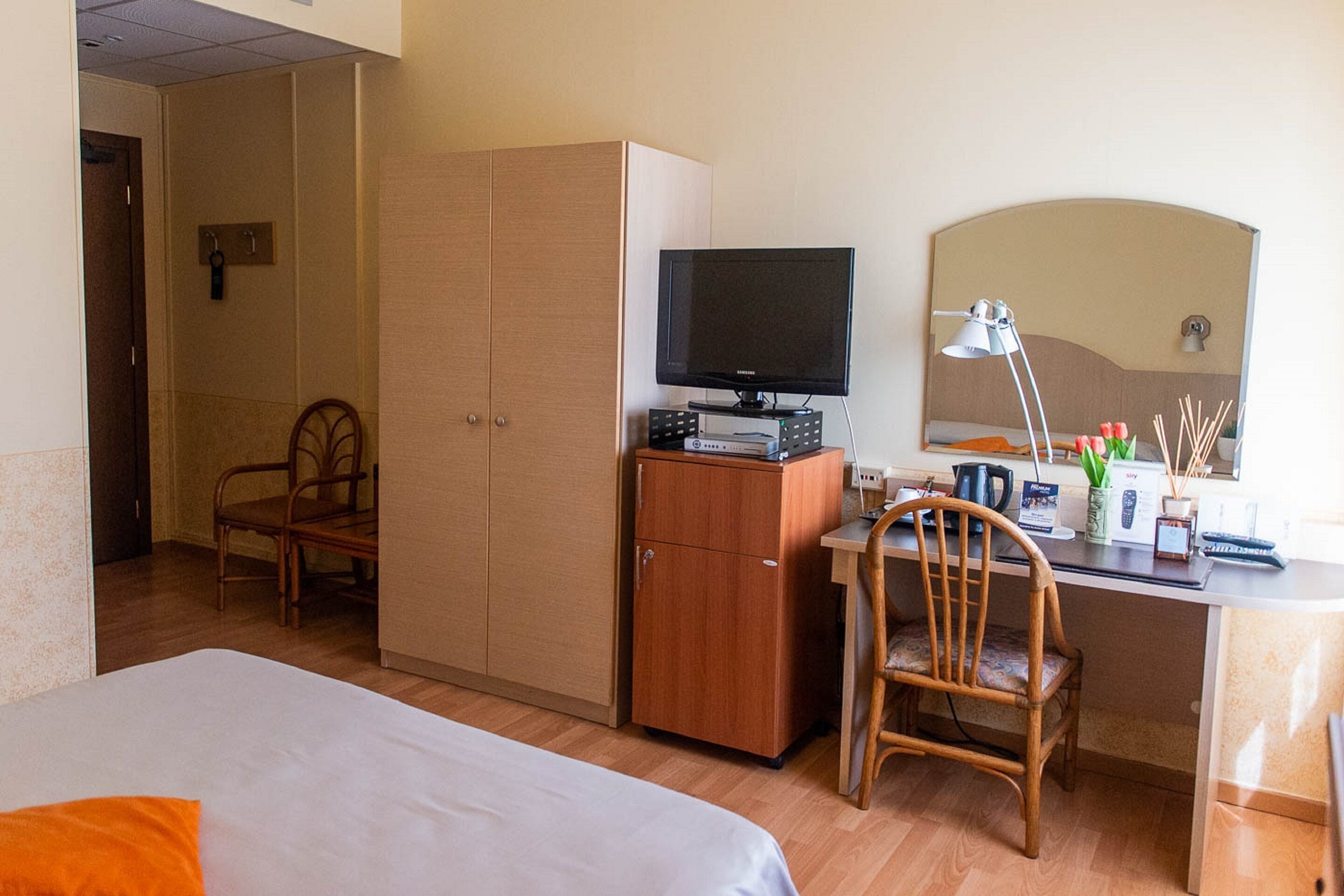 A hotel room with a bed, a desk with a computer, a television, a mirror, and a wardrobe.