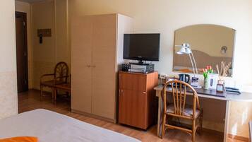 Habitación de hotel con cama, escritorio con computadora, televisor, espejo y armario.