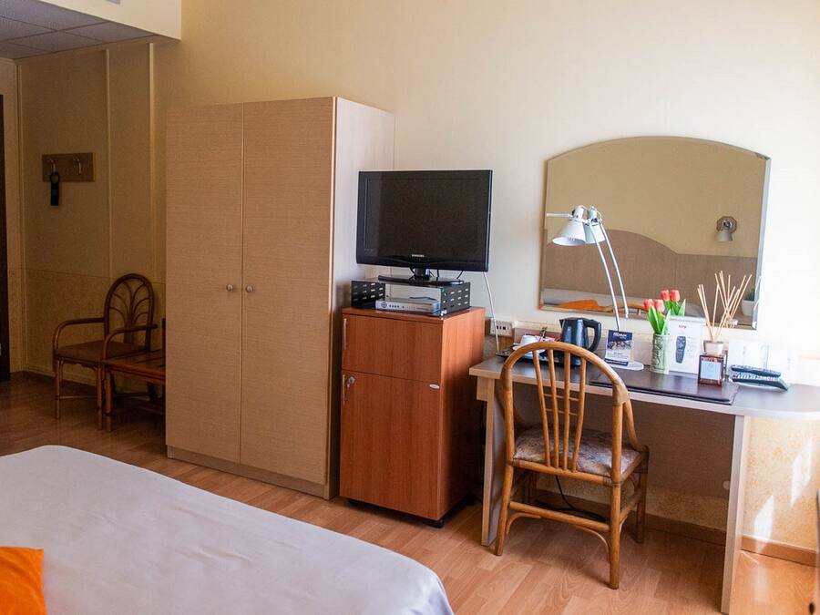 Habitación de hotel con cama, escritorio con computadora, televisor, espejo y armario.