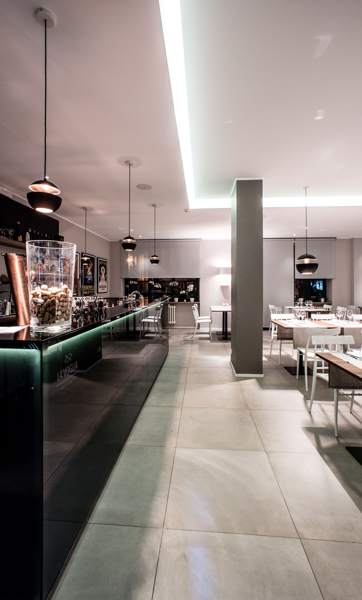 Un interno ristorante moderno con zona bar, posti a sedere e illuminazione a sospensione.