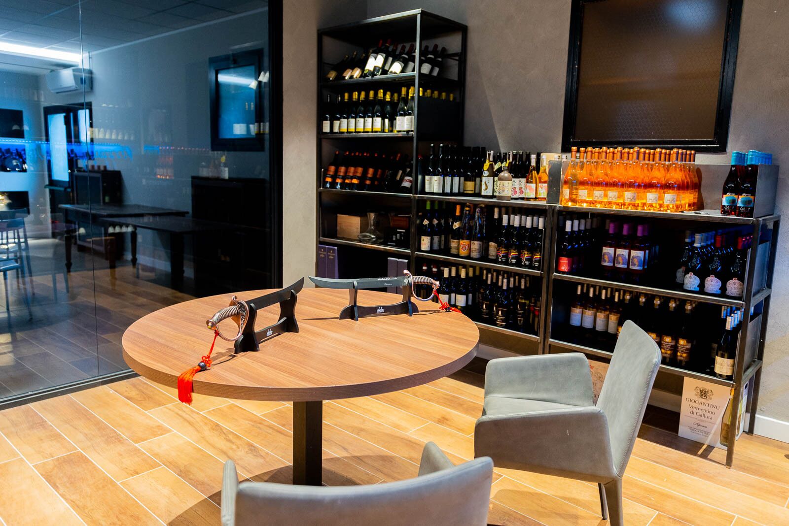 A modern bar area with a round wooden table, two chairs, and a wine rack filled with various bottles.