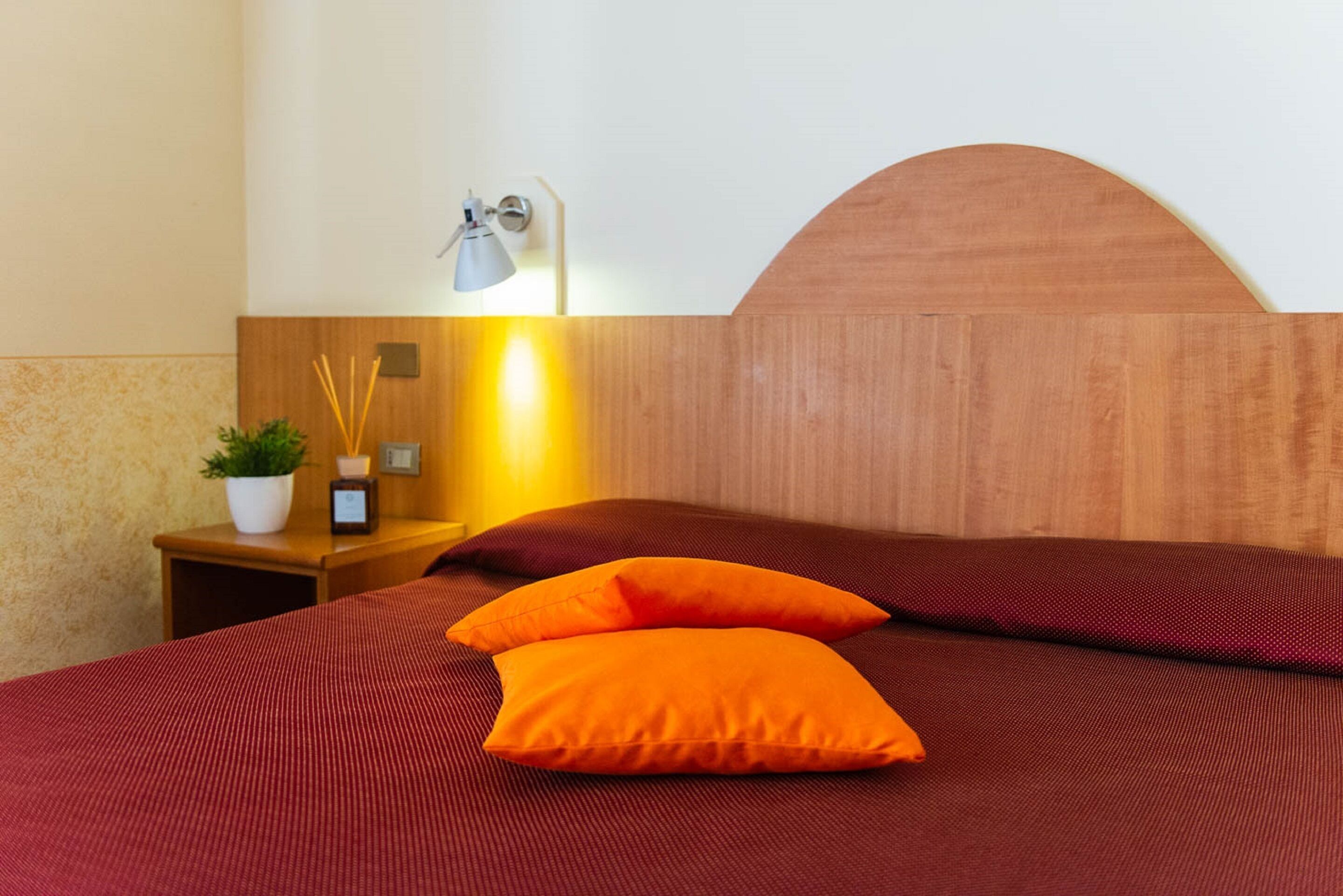 A neatly made bed with a wooden headboard and two orange pillows.