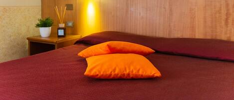 A neatly made bed with a wooden headboard and two orange pillows.