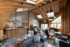 A rustic interior with a stone wall bar, leather seating, and large windows. - Maison Saint Jean (Courmayeur)