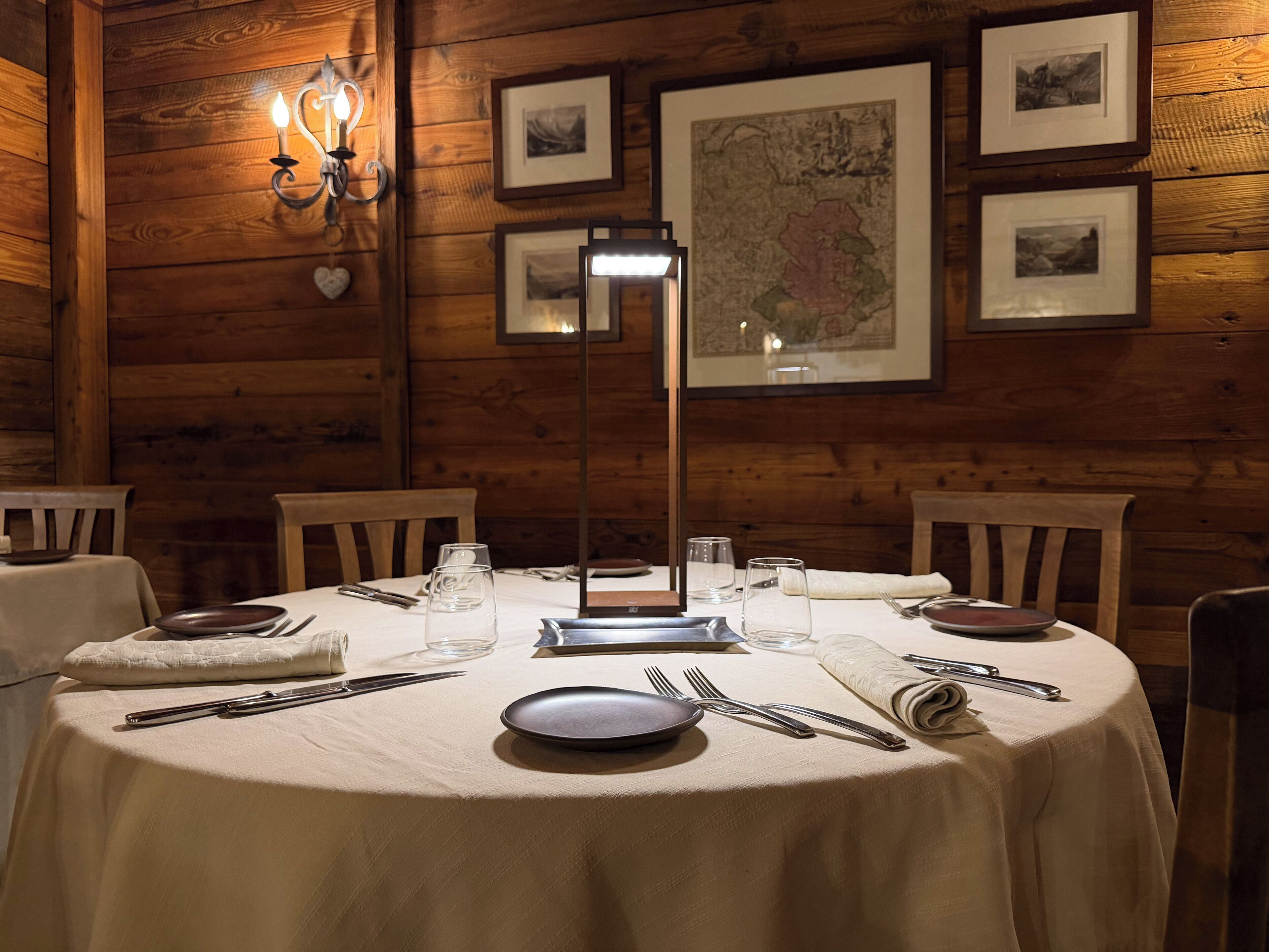 A wooden-paneled room with a round table set for dining, framed pictures on the wall, and a map.