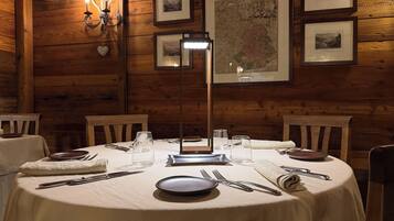 A wooden-paneled room with a round table set for dining, framed pictures on the wall, and a map.