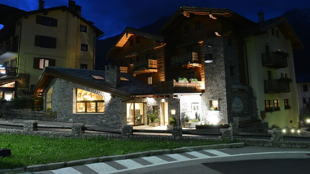 A hotel with a stone facade, wooden balconies, and a lit entrance. - Maison Saint Jean (Courmayeur)