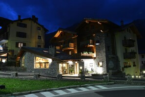 Un hotel con fachada de piedra, balcones de madera y una entrada iluminada.