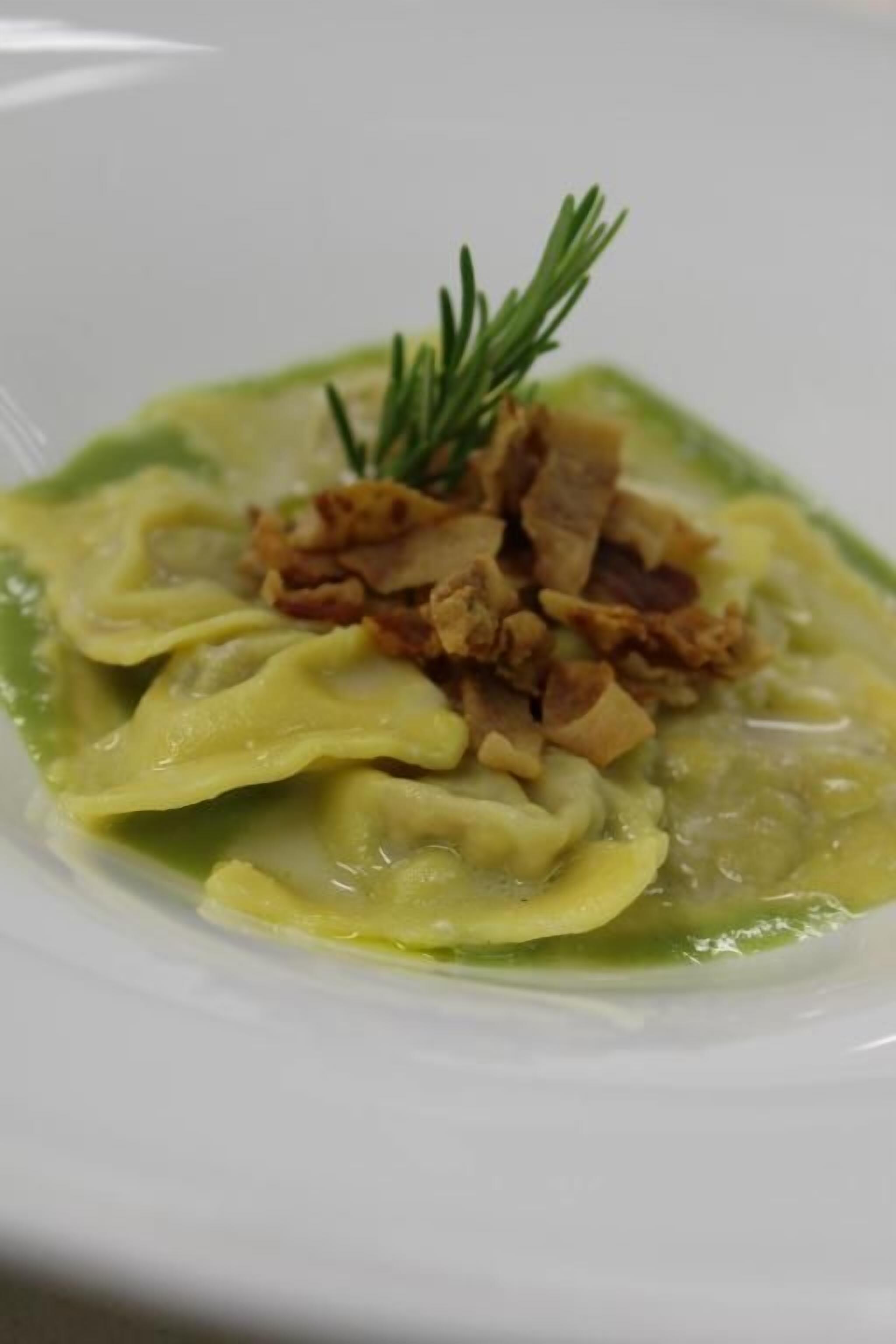A plate of ravioli with a garnish of rosemary and crispy bacon.