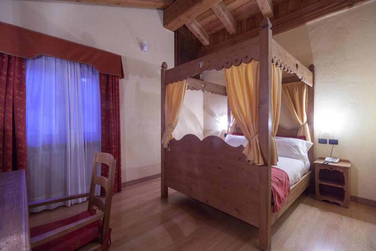 A wooden four-poster bed with curtains, a bedside table with a phone, and a chair.