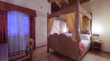 Un lit à baldaquin en bois, agrémenté de rideaux, une chaise et une table de chevet avec une lampe.