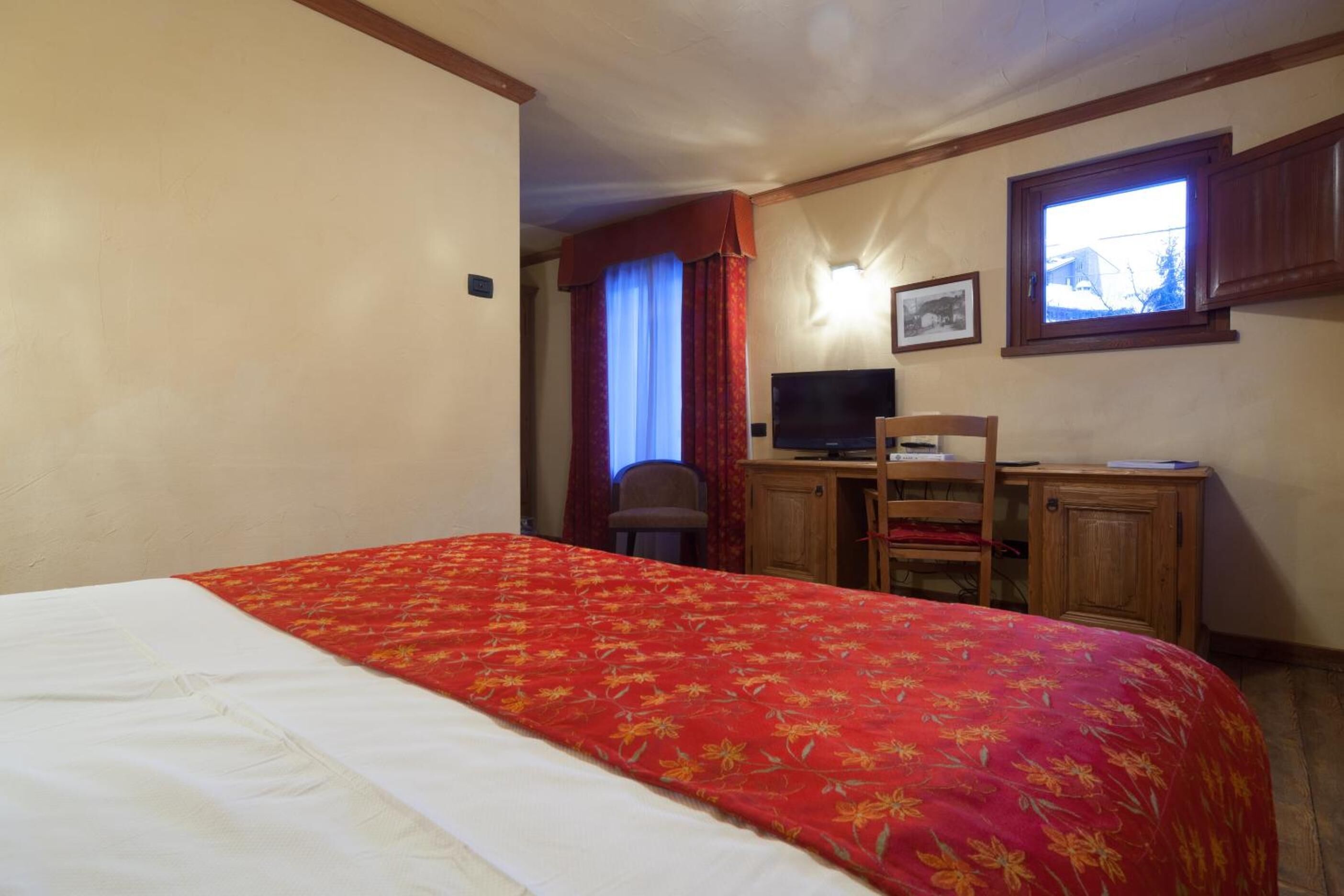 Ein Hotelzimmer mit einem Bett, einem Schreibtisch mit Computer, einem Stuhl und einem Fenster.
