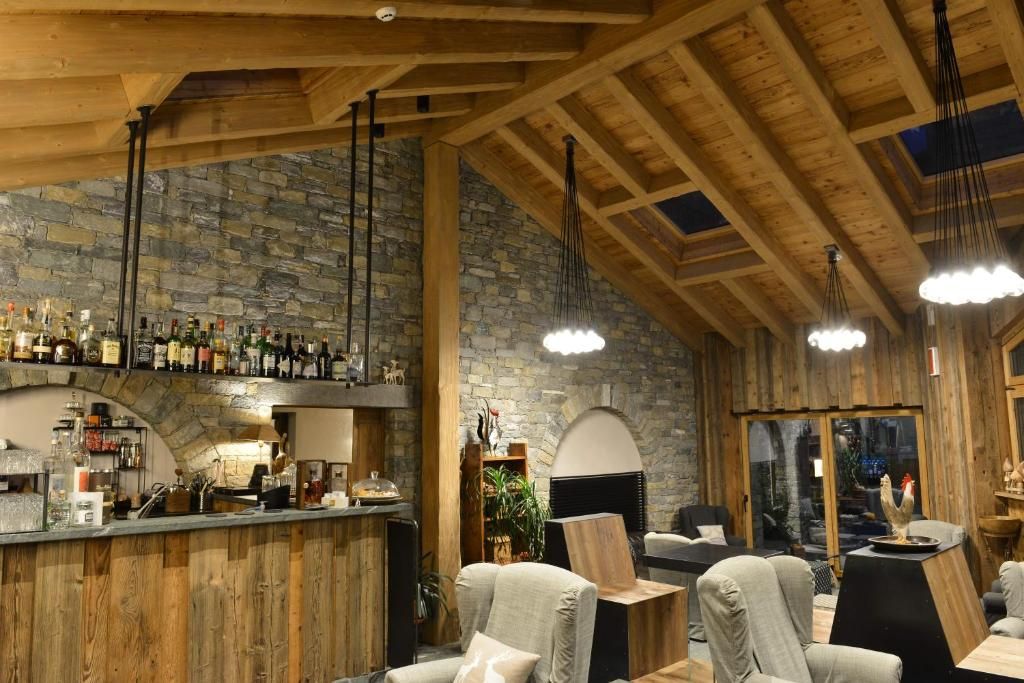 Um interior rústico com área de bar, paredes de pedra, vigas de madeira e luminárias pendentes.