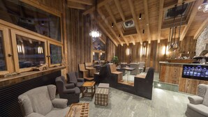 A spacious living area with wooden walls, a stone fireplace, and a large TV screen. - Maison Saint Jean (Courmayeur)