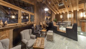 A modern interior with wooden beams, a seating area with sofas and a coffee table, and a bar area with stools. - Maison Saint Jean (Courmayeur)