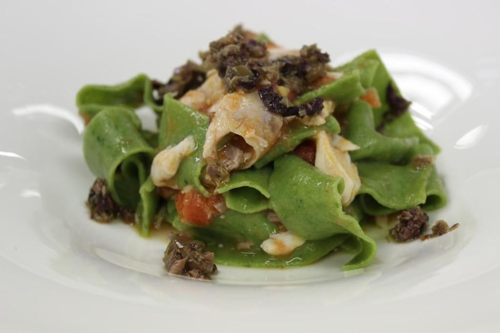 Un plato de comida con hojas verdes, tomates y un aderezo que parece ser una mezcla de carne y posiblemente nueces.