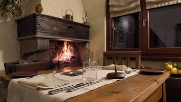 A dining table set with cutlery and glasses, a fireplace with a visible fire, and a window with curtains.