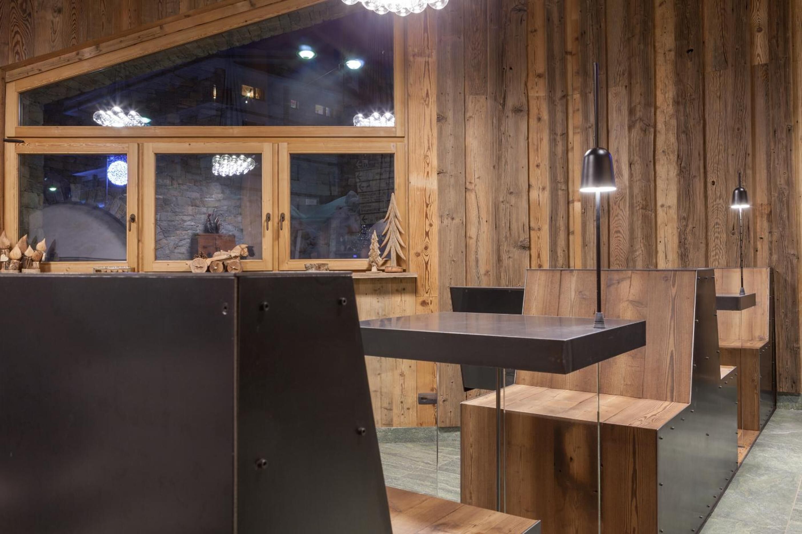 Un interior moderno con paredes de madera, un ventanal grande y una zona de comedor con mesa y sillas.