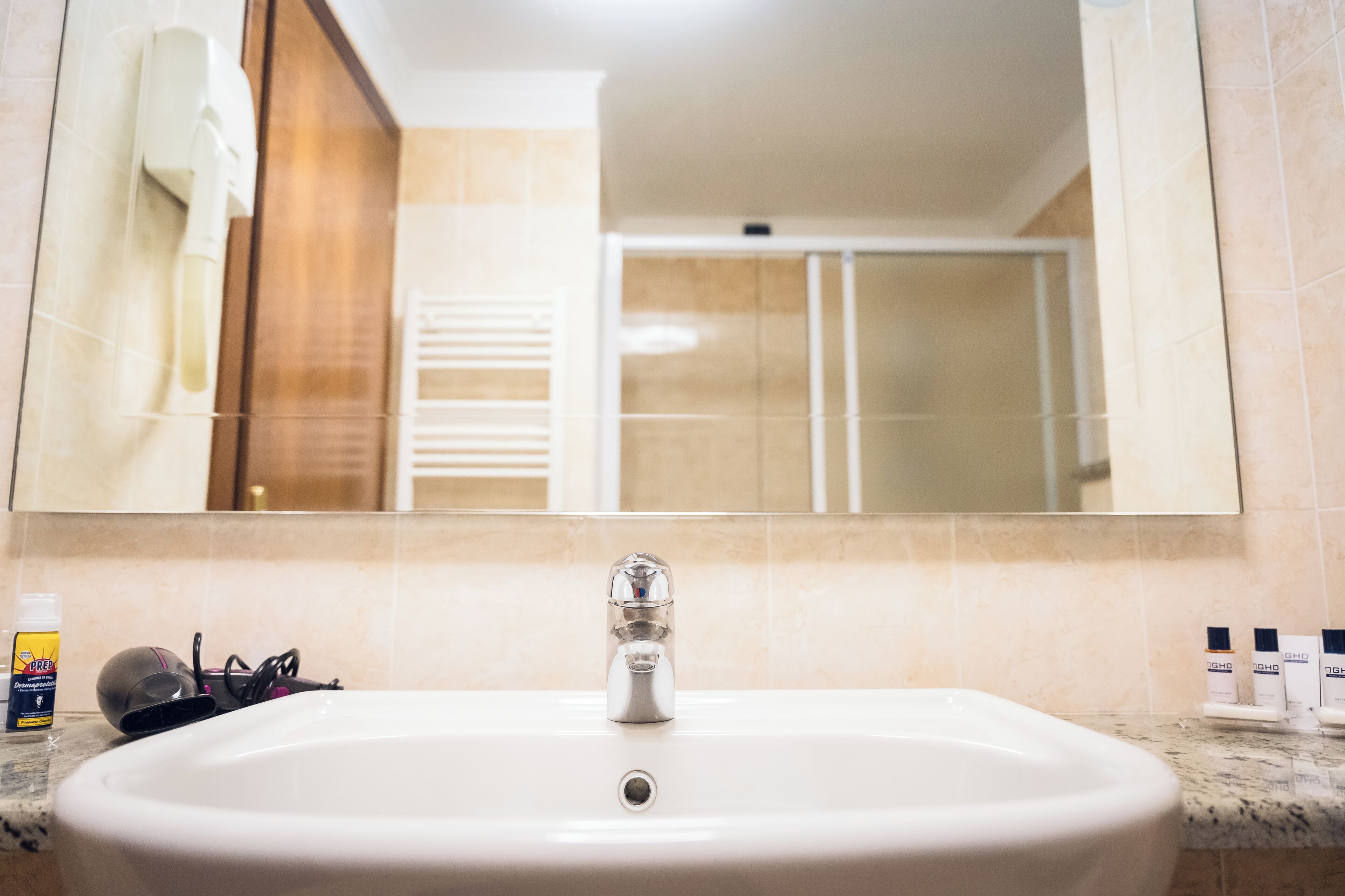 Un baño con lavamanos, espejo y artículos de aseo sobre el mostrador.