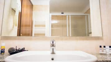 Un baño con lavamanos, espejo y artículos de aseo sobre el mostrador.