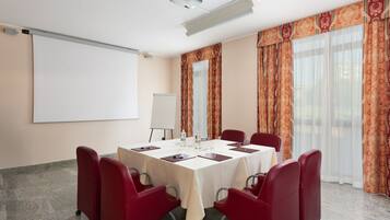 Una sala conferenze con lavagna, proiettore, tavolo e sedie, e ampie finestre con tende.
