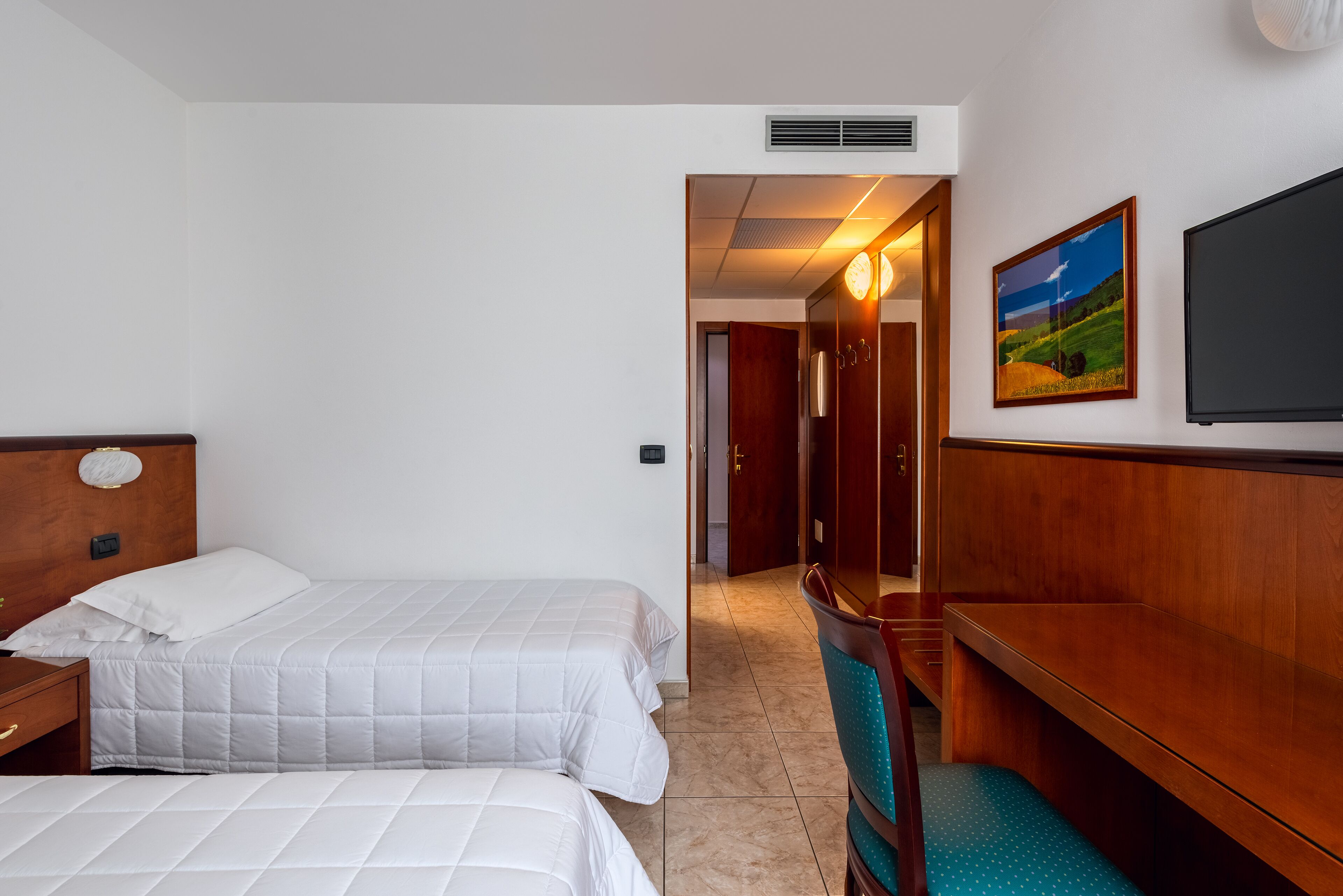 Habitación de hotel con dos camas, un banco de madera, un televisor y un cuadro en la pared.