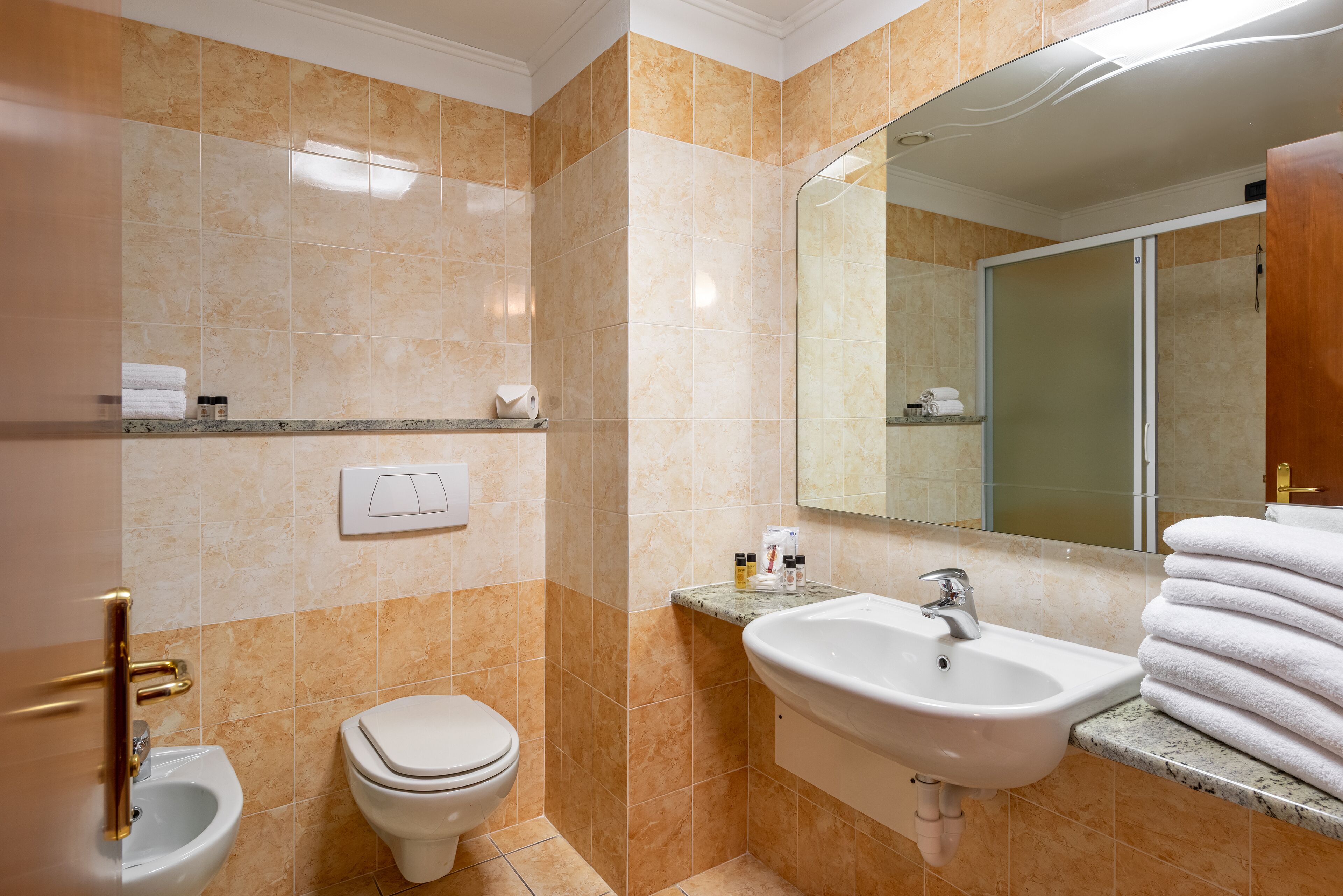 Un baño con inodoro, bidé, lavamanos y espejo.