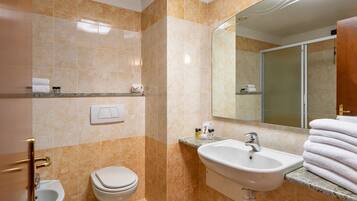 Un baño con inodoro, bidé, lavamanos y espejo.