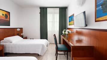Habitación de hotel con dos camas, un escritorio, una silla, un televisor y obras de arte en las paredes.