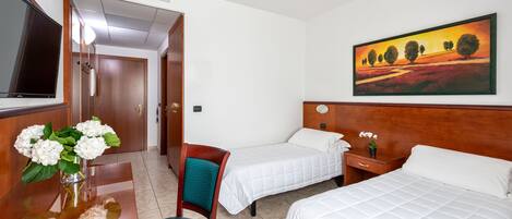 Une chambre d’hôtel avec deux lits, une télévision, un bureau agrémenté d’un vase de fleurs et un tableau au mur.