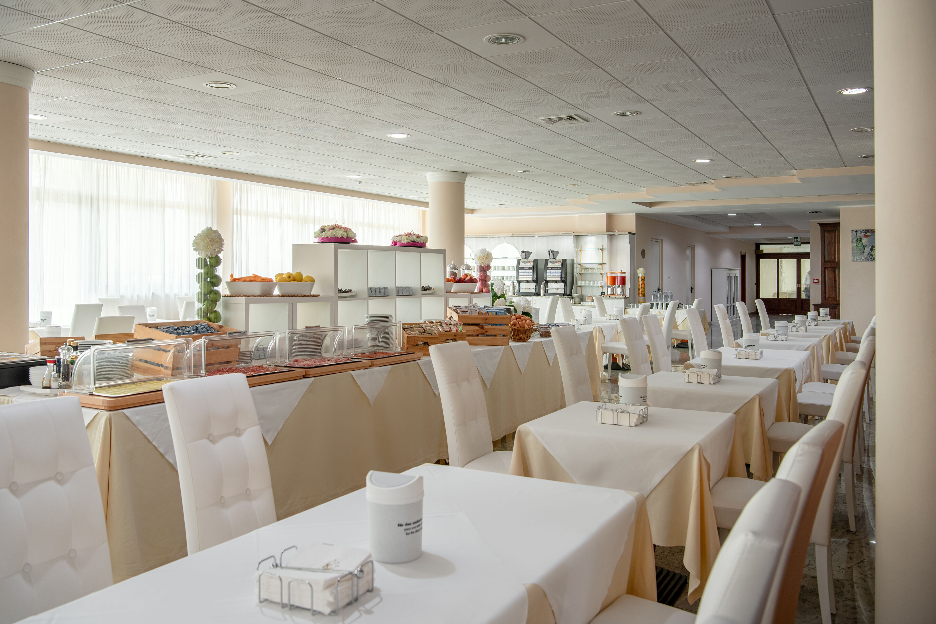 A spacious dining area with multiple tables and chairs, a buffet with various food items, and a clean, modern interior.