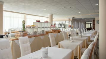 A spacious dining area with multiple tables and chairs, a buffet with various food items, and a clean, modern interior.
